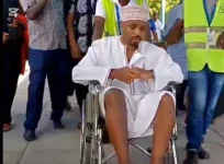 Frail Mwangi limps into airport on stretcher.webp